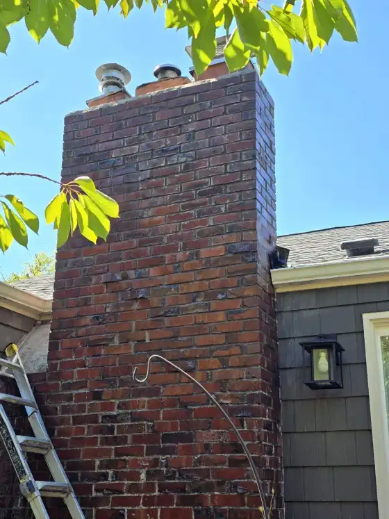 The same brick chimney after cleaning, with clean red brick and several flue pipes on top