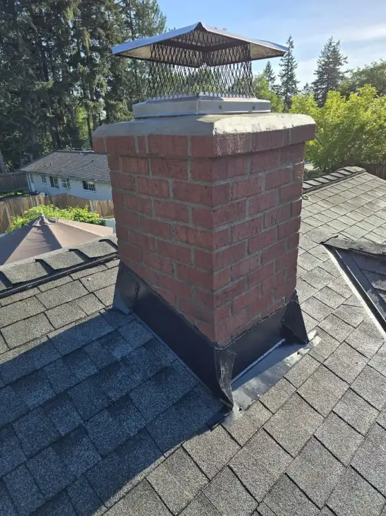 Red brick chimney with a fresh crown, black flashing and a stainless steel mesh cap on a dark shingle roof