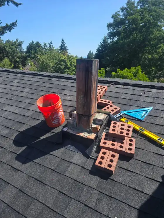 Chimney flue above the roof with new bricks stacked beside it and fresh mortar at the base