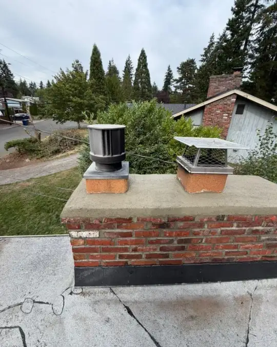Flat-roof chimney after repair with a new tan crown under a stainless steel cap and a gray cap