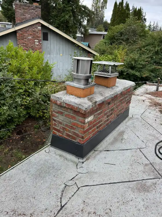 Same flat-roof chimney from the side, showing the old worn crown and black flashing, before repair