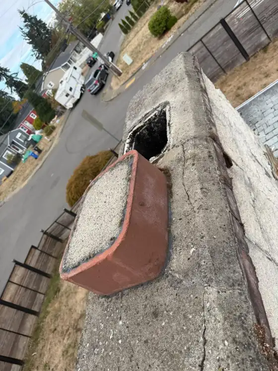 Chimney crown with cracks and a broken flue tile opening, seen from above with a street below