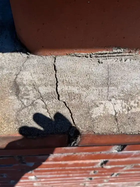 Close view of a crack running across a chimney crown beside the flue tile