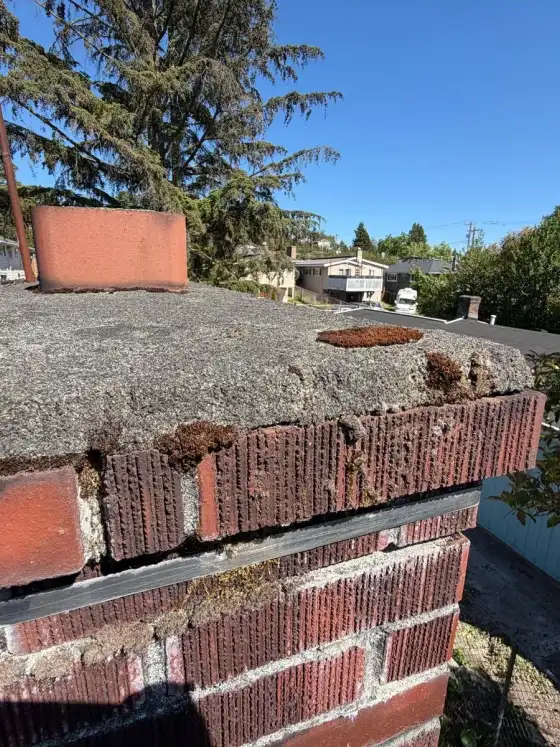 Crumbling edge of a chimney crown above old brick on a flat roof