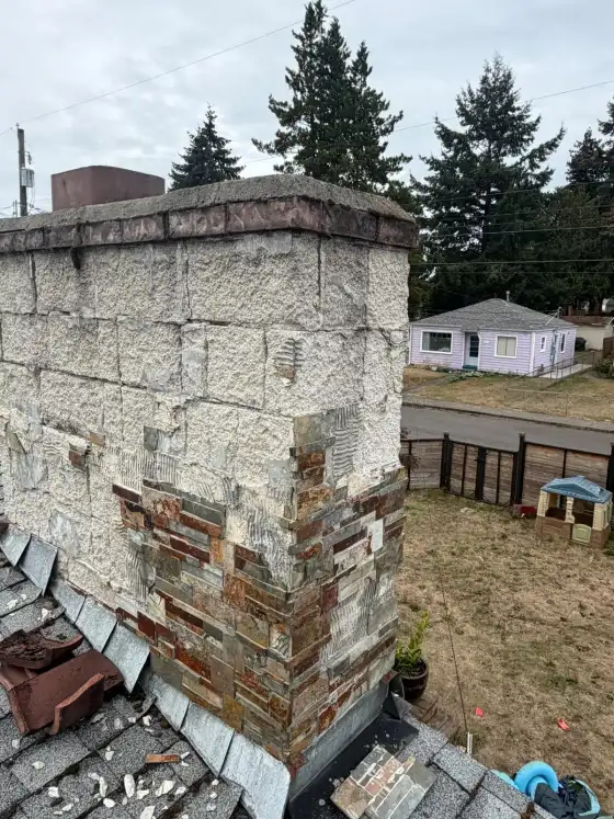 Chimney with white stucco blocks peeling away from stone veneer and debris on the roof below