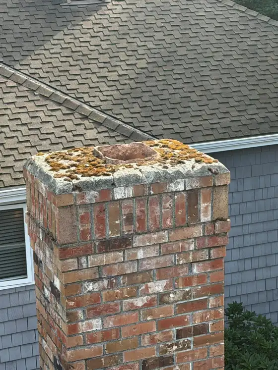 Brick chimney with a mossy, worn crown beside a gray house