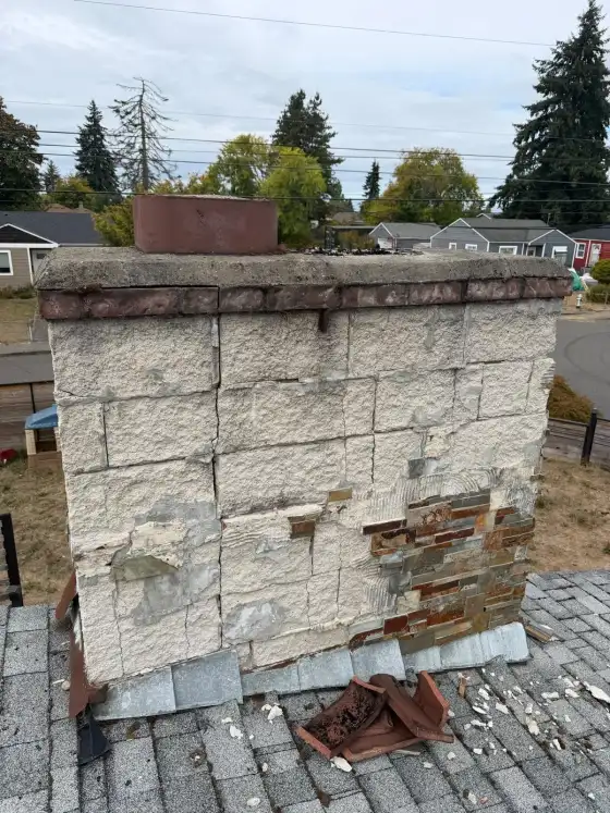 Front of a chimney with peeling white stucco blocks and exposed stone