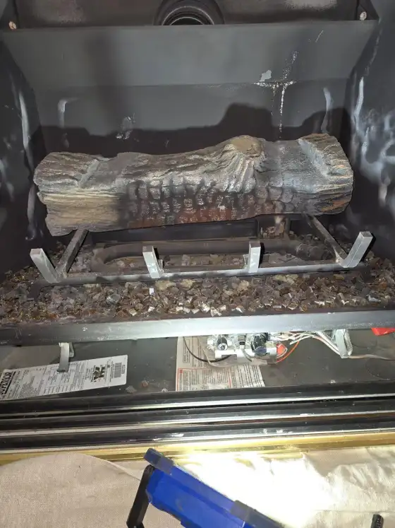 Opened gas fireplace showing the log set, the burner and the pilot assembly below