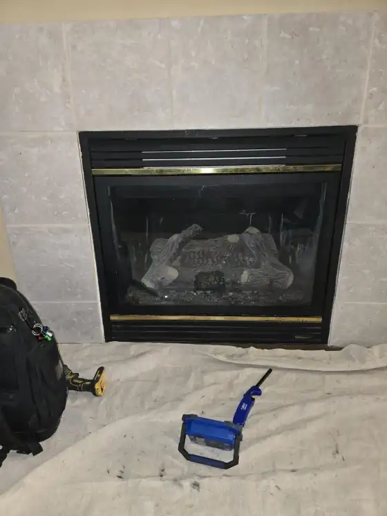 Gas fireplace with a brass trim surround, drop cloth and tools set out on the floor for service