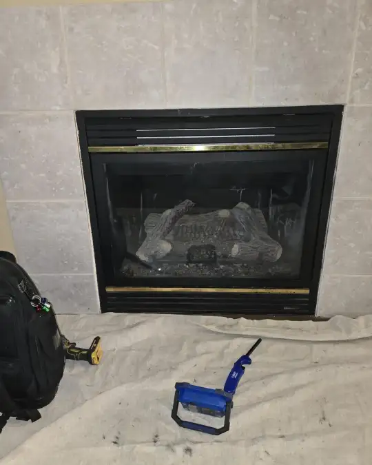 Gas fireplace with a brass trim surround, drop cloth and tools set out on the floor for service