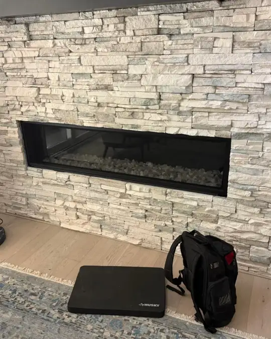 Linear gas fireplace with glass front set into a light stacked stone wall