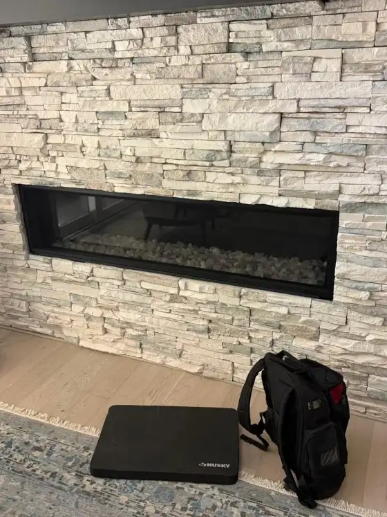 Linear gas fireplace with glass front set into a light stacked stone wall