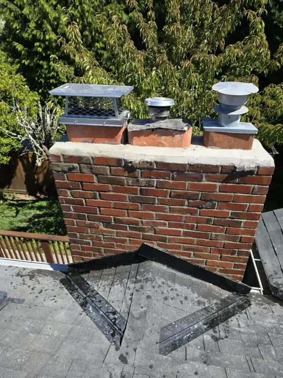 Brick chimney with three caps and a metal vent next to a wooden deck