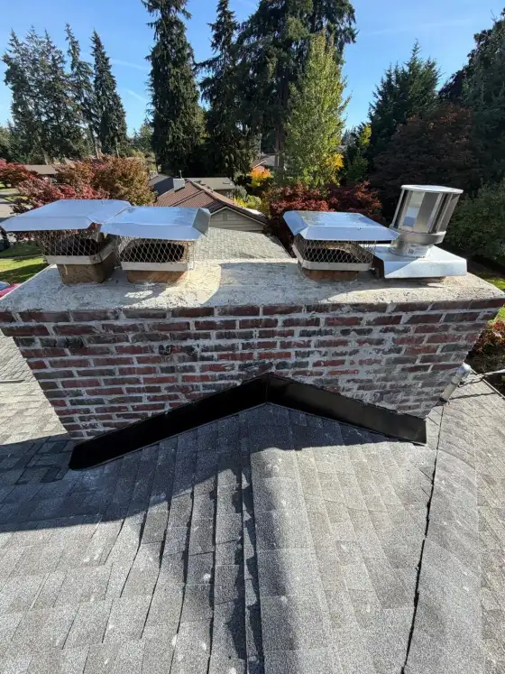 Wide brick chimney with several stainless steel caps and a metal vent cap on the roof