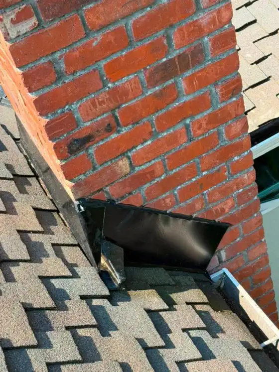 Black step flashing at the corner of a brick chimney, seen at an angle