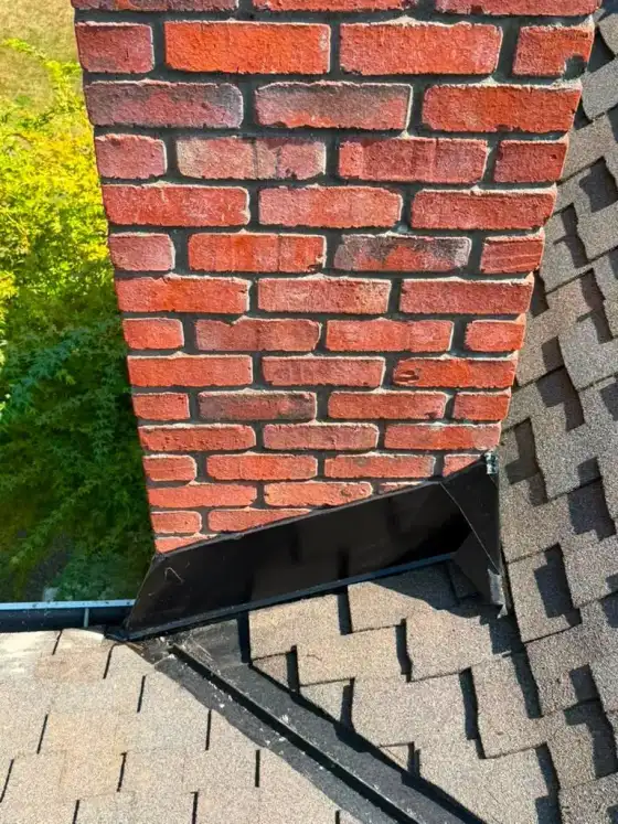 Red brick chimney with black step flashing where it meets the shingle roof