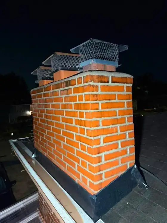 Brick chimney at night with a new crown and two stainless steel caps, lit from the side