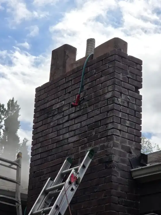 Dark brick chimney with a hose and spray mist at the top while it is being washed