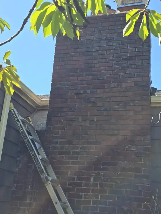 Brick chimney half cleaned, with a clean lighter streak next to the dark soot-stained brick