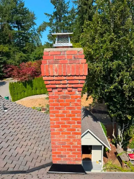 Tall red brick chimney with a corbelled top and a stainless steel cap, with a garden shed below