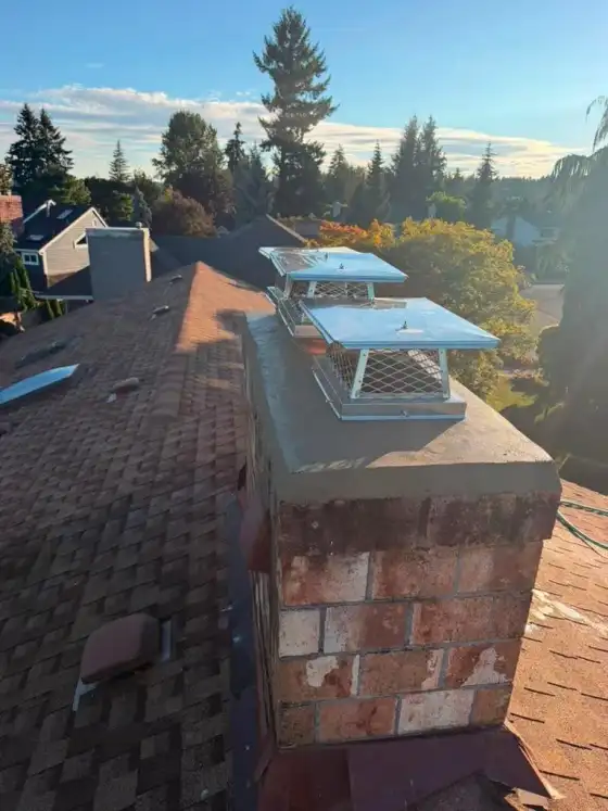 Two stainless steel mesh caps on a new gray crown on a brick chimney on an orange-brown shingle roof